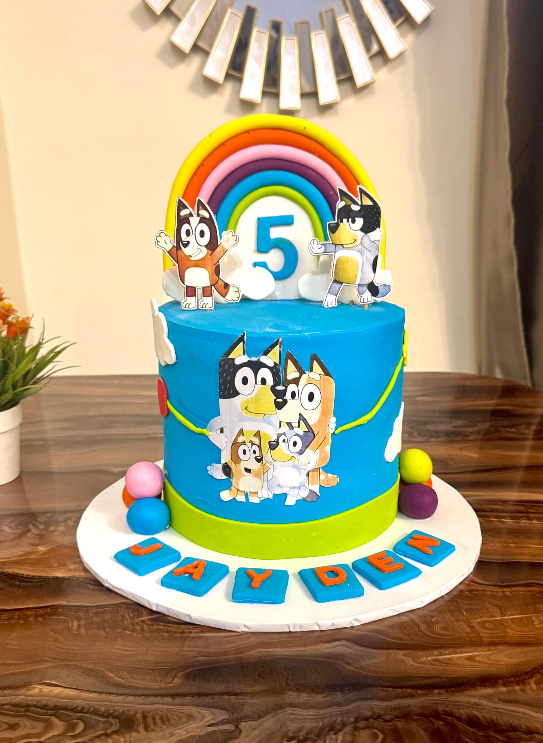 Bluey Kids Birthday Cake Bluey cartoon-themed kids birthday cake with rainbow topper and character decorations in Abuja by Cakes by Teez