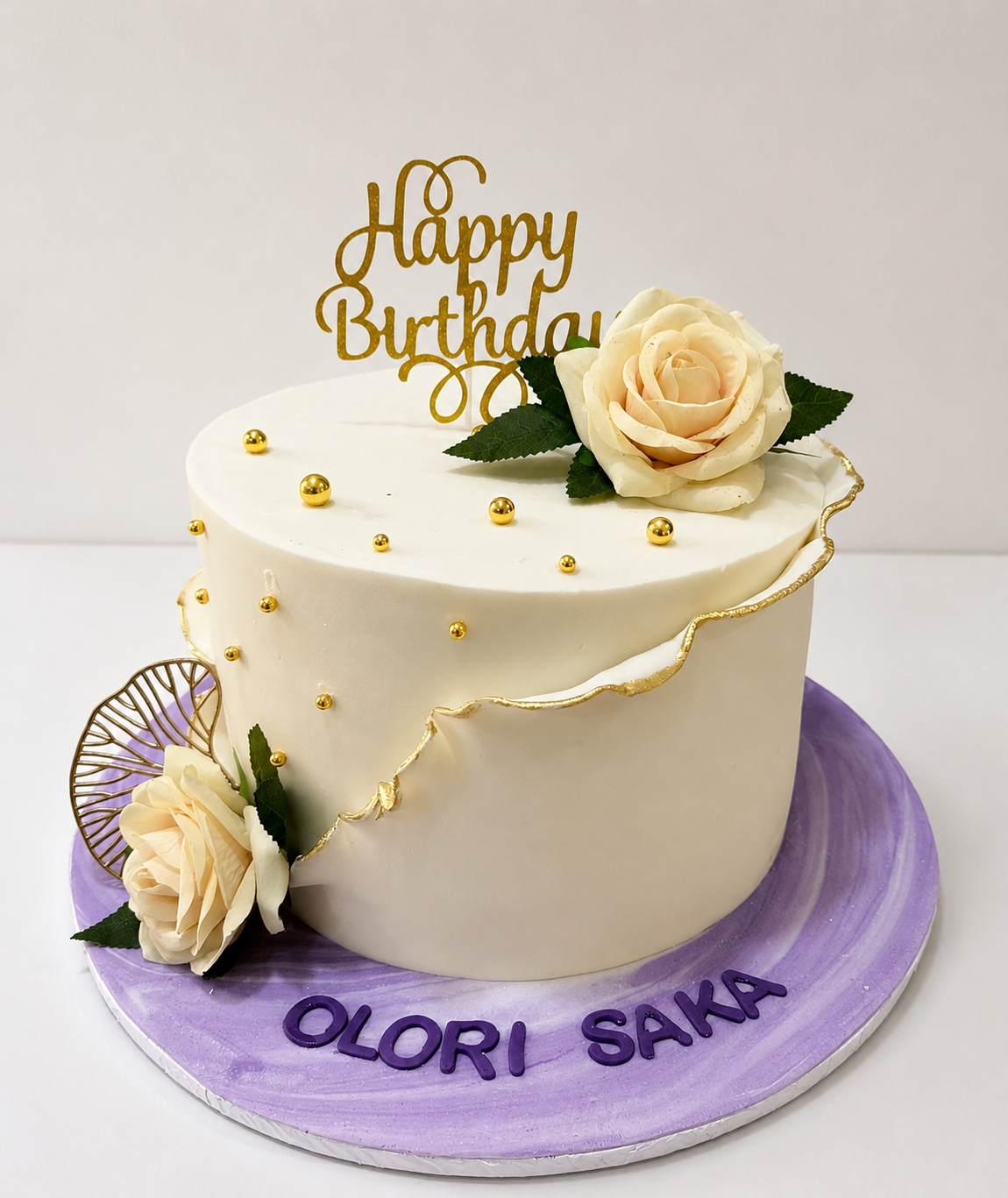 Ivory buttercream birthday cake with gold bead cascade, gold leaf crack detail, and cream roses by Cakes by Teez in Abuja