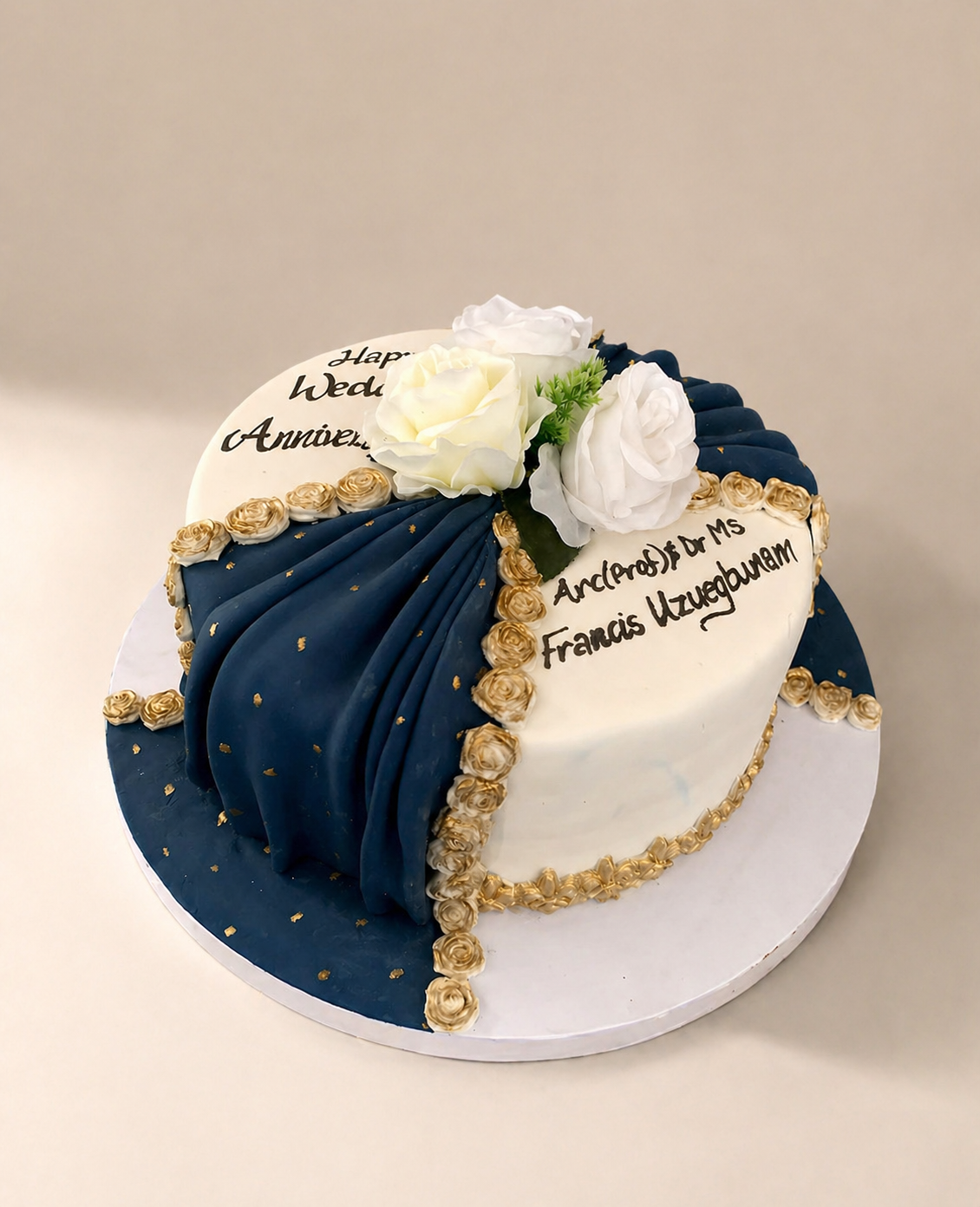 Navy blue and gold fondant wedding anniversary cake with draped fabric effect and white roses by Cakes by Teez in Abuja