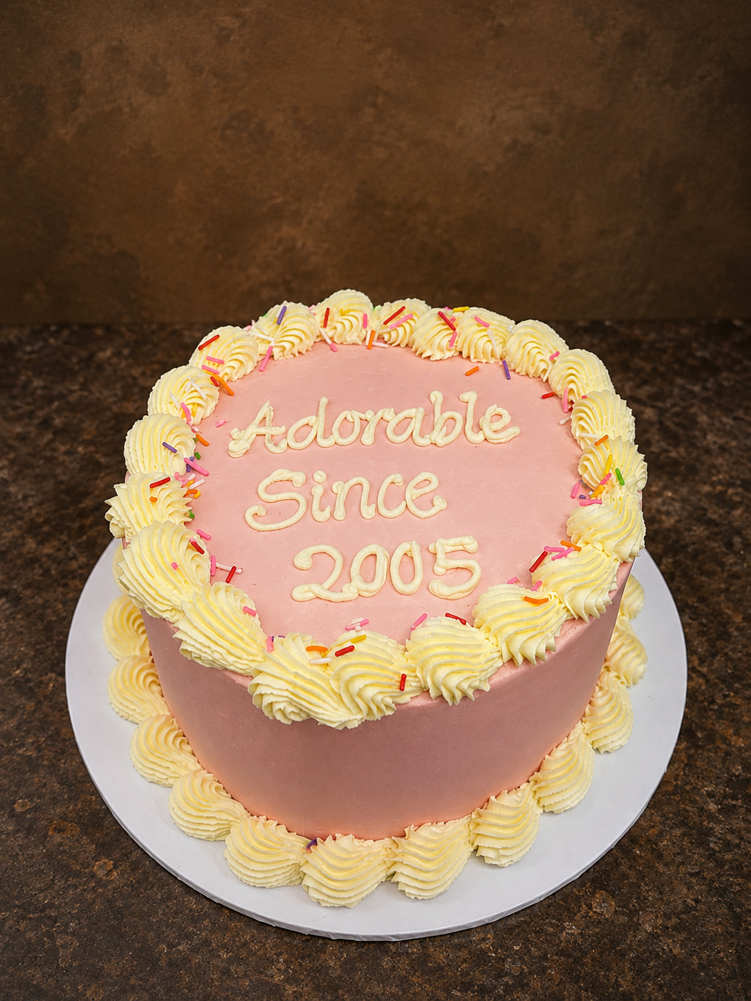 Pink buttercream birthday cake with yellow shell piping border and colourful sprinkles by Cakes by Teez in Abuja