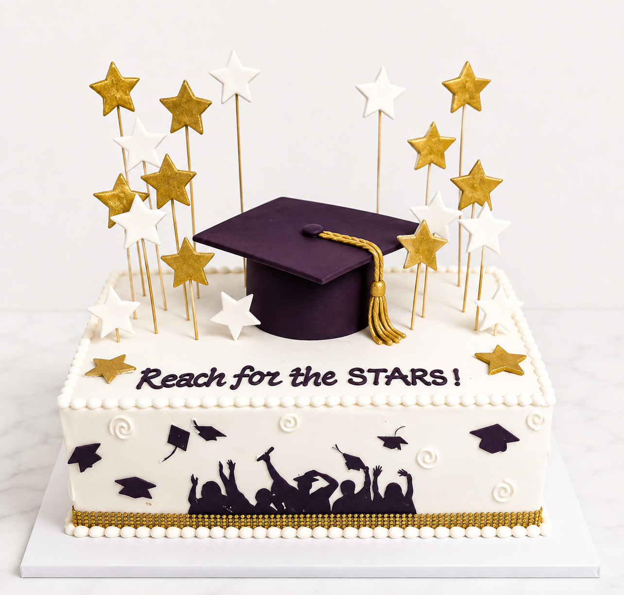 White fondant graduation cake with a purple fondant graduation cap topper, gold and white fondant stars, and a silhouette of graduates by Cakes by Teez in Abuja