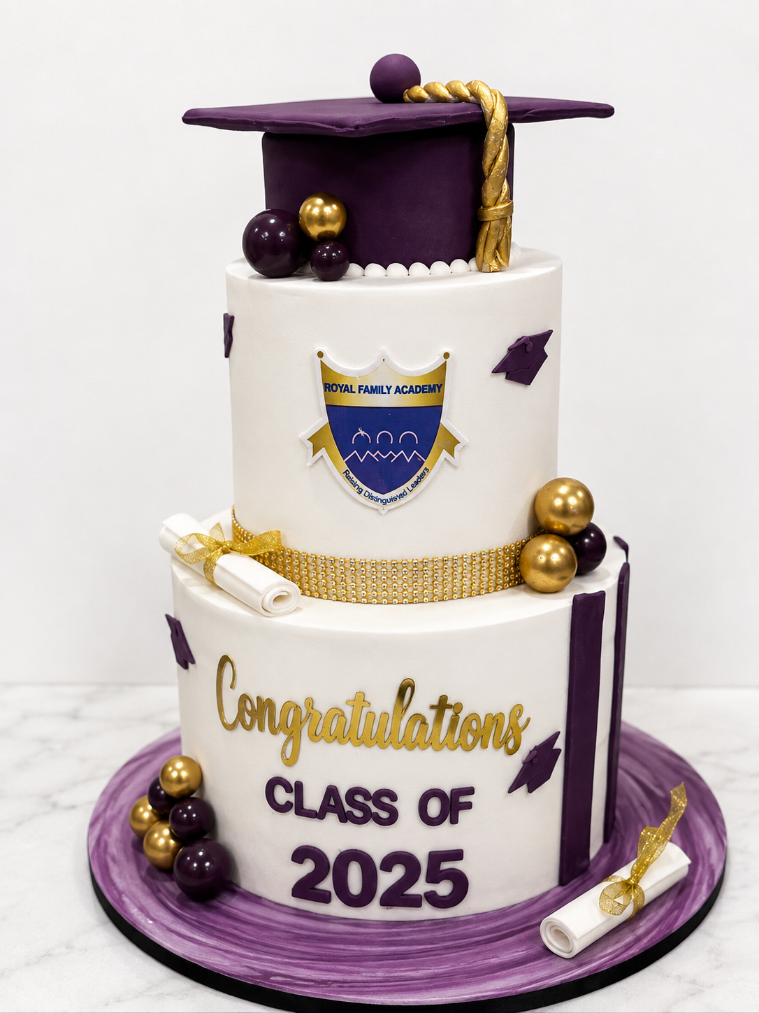 Two-tier purple and white fondant graduation cake with a fondant graduation cap, gold spheres, and a school crest topper by Cakes by Teez in Abuja