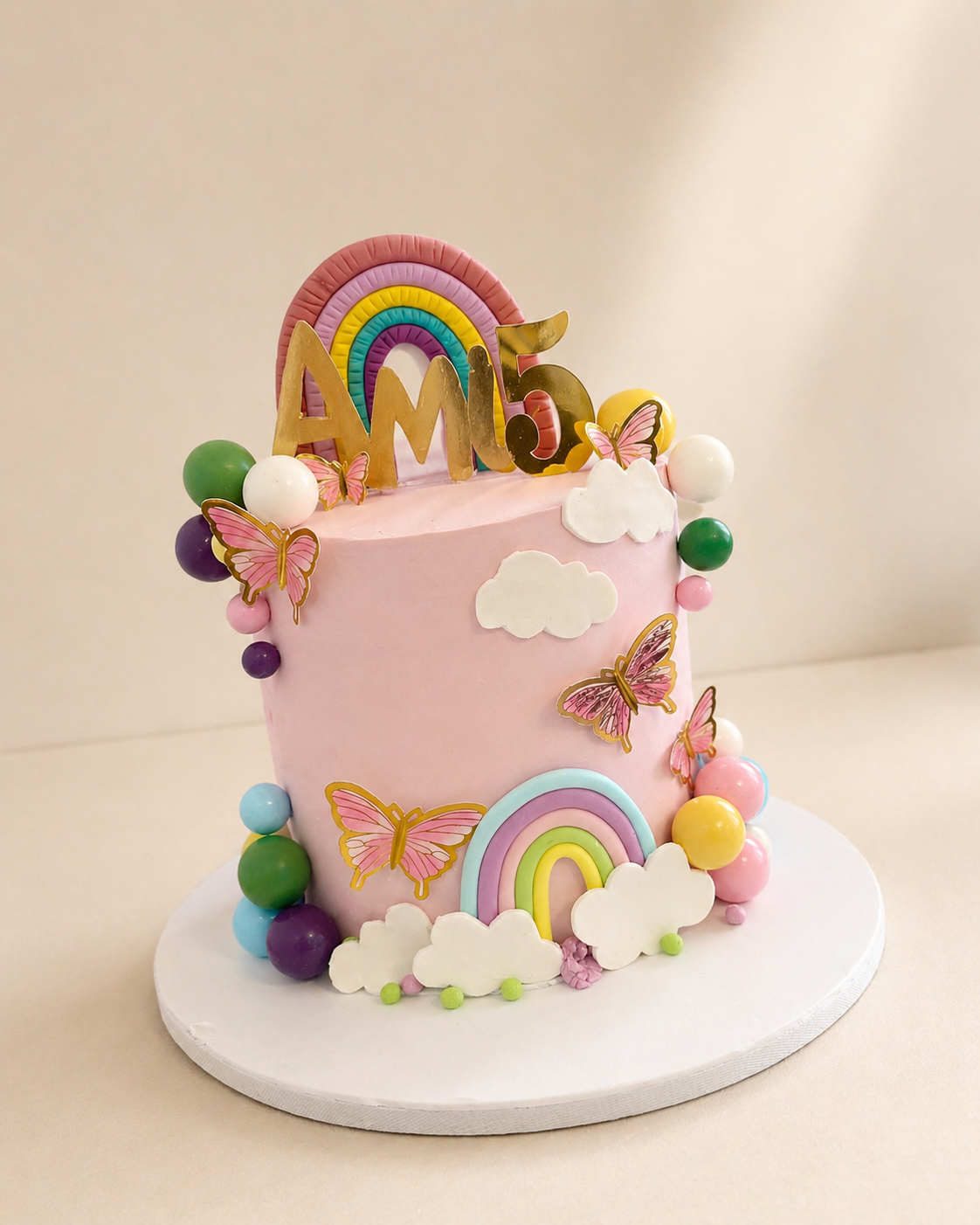 Pink pastel rainbow and butterfly birthday cake with colourful balloon garland decorations by Cakes by Teez in Abuja
