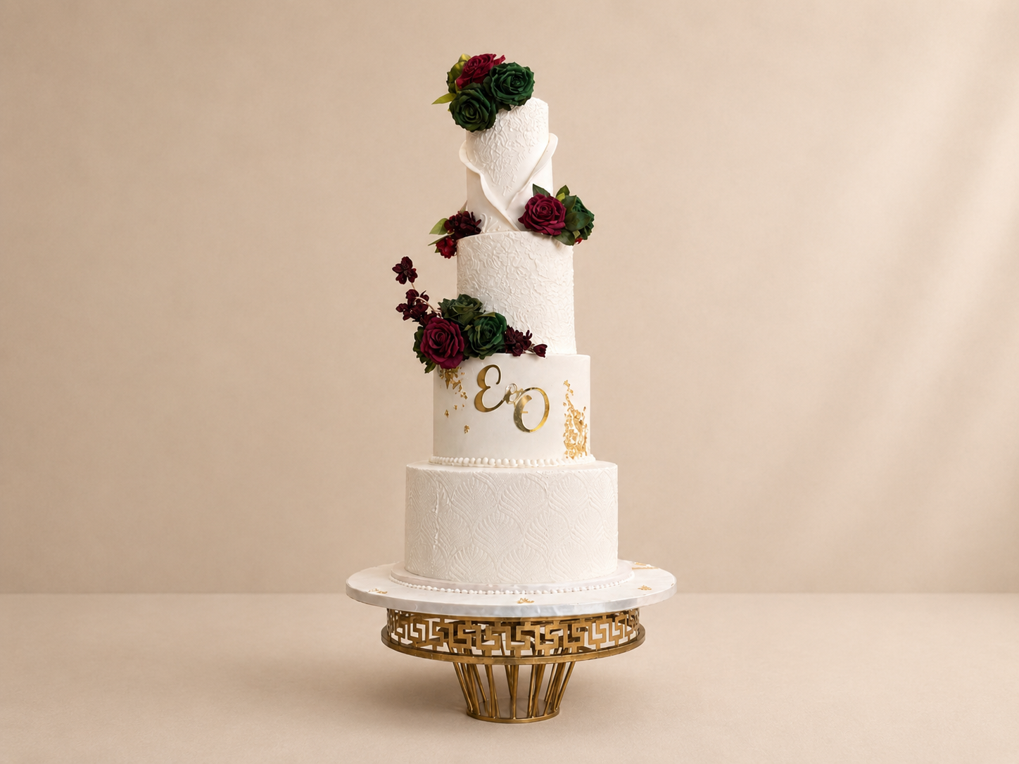 Wedding Cakes Three-tier white wedding cake with burgundy roses and gold monogram on ornate stand by Cakes by Teez in Abuja