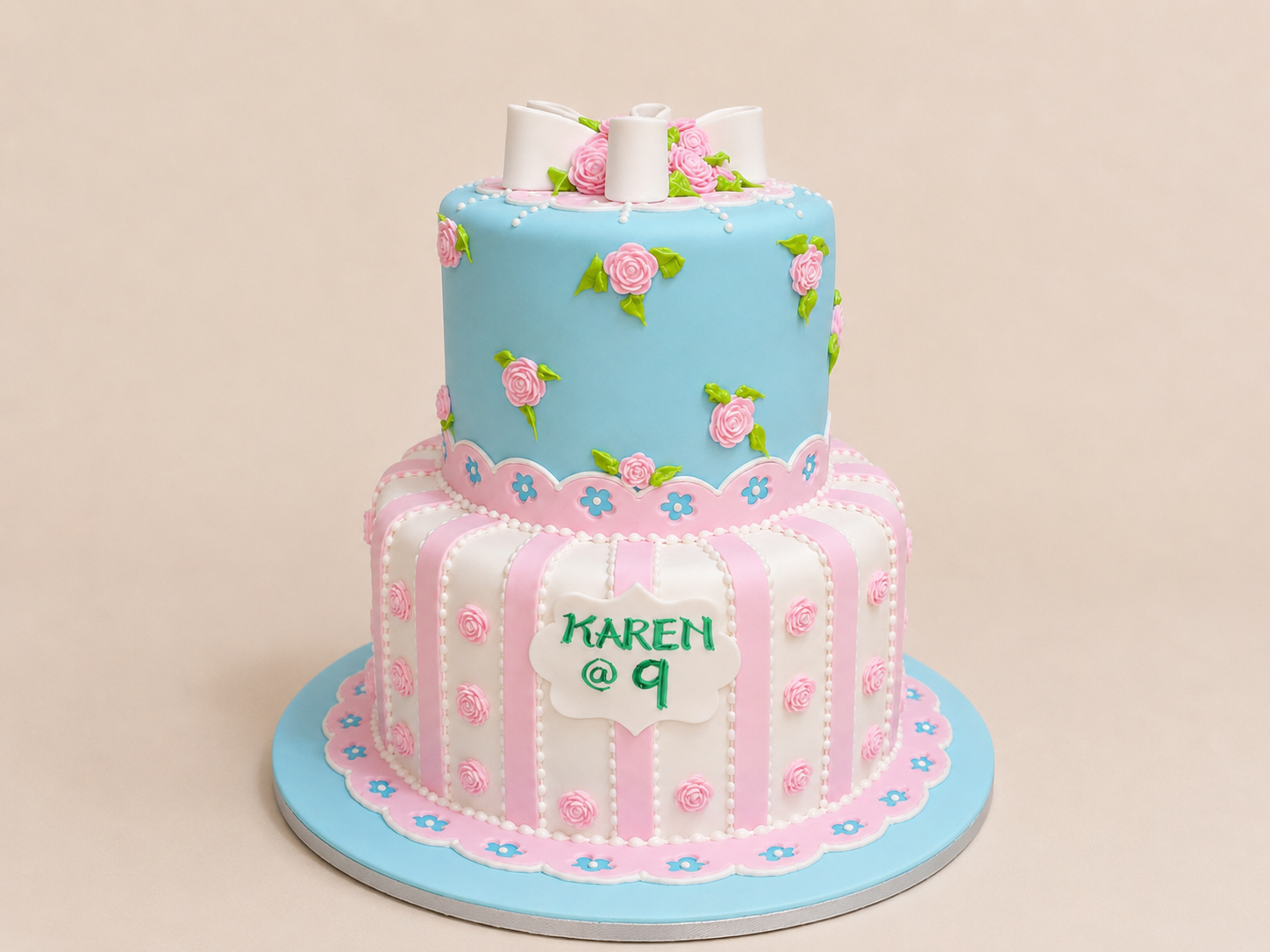 Two-tier pastel pink and blue vintage girls birthday cake with ribbon bow and floral details by Cakes by Teez in Abuja